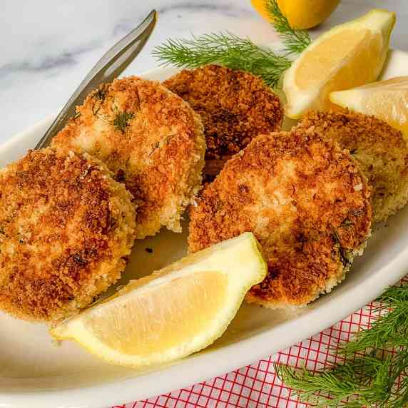 close up of chicken cakes with lemon & dill on a white plate