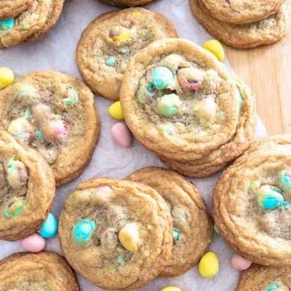 Cadbury egg cookies on a sheet of parchment paper with mini eggs scattered around the cookies.