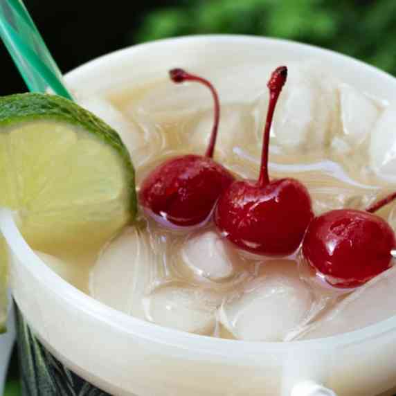 Close up of a bucket of tropical rum punch garnished with cherries and lime.