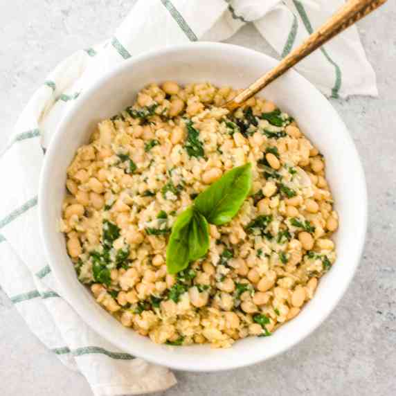 Cauliflower rice and white navy beans risotto in almond sauce topped with basil leaves served in whi