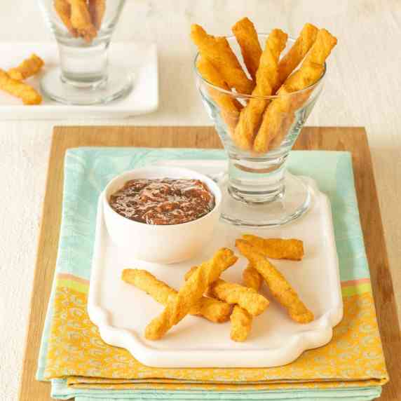Glass holding cheese straws atop a white platter, with pepper jelly on the side