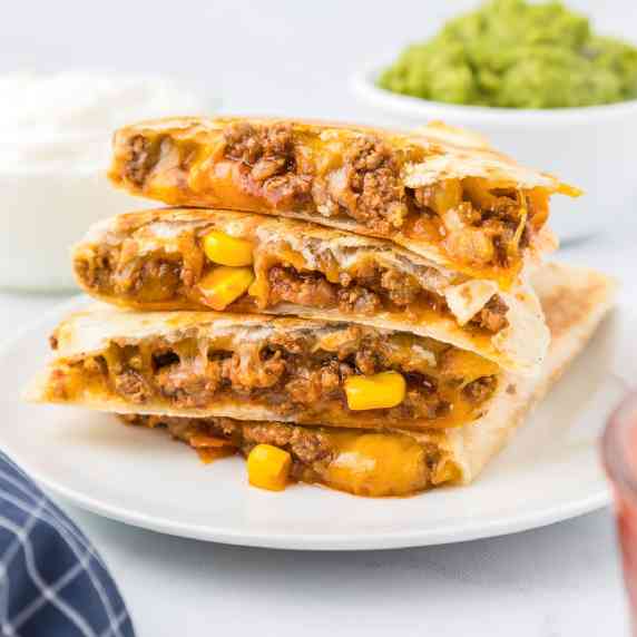 Side view of four quesadillas stacked on a plate to show the beef, corn and cheesy filling.