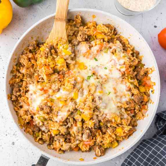 View of a deconstructed stuffed pepper rice and cheese dish in a large skillet from overhead. 