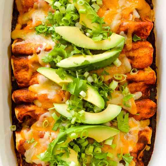 Cheesy chicken enchiladas with red sauce topped with slices of avocado.