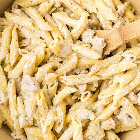 Super close up square view of chicken penne alfredo being stirred with a wooden spoon.