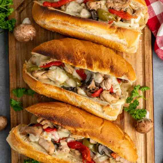 Chicken Philly cheesesteaks on a wood cutting board.