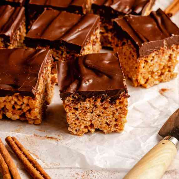 An array of chocolate covered rice krispie treats cut up on parchment with a knife to the side.