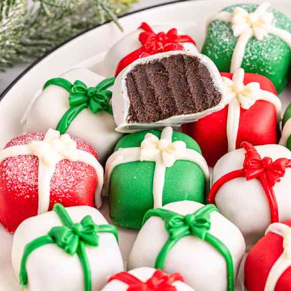 A plate full of Christmas chocolate truffles decorated like presents with one missing a bite.