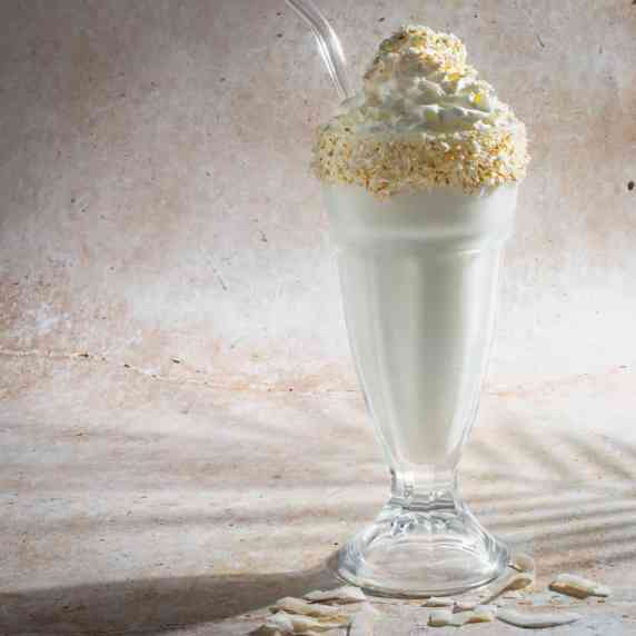 Coconut milkshake in a tall milkshake glass with a glass straw.