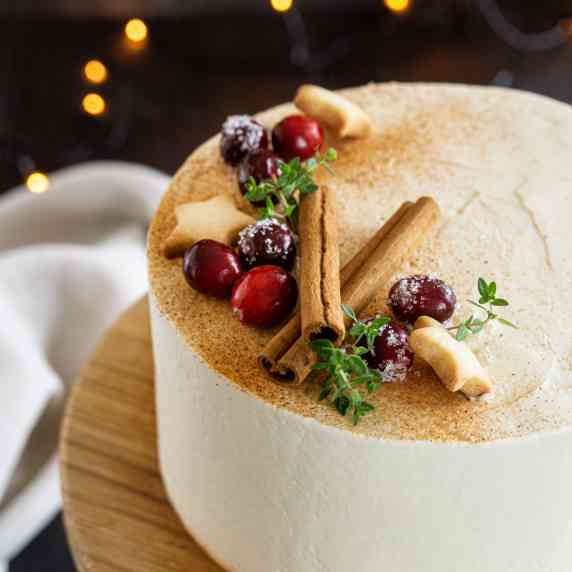 Close up of a cranberry honey cake decorated with fresh cranberries, cinnamon sticks and thyme twigs