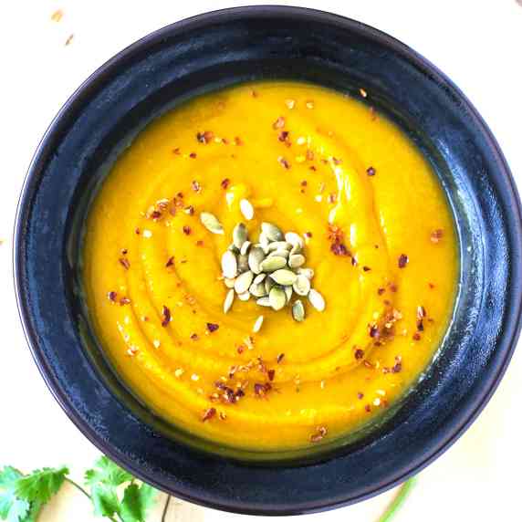 Pureed Butternut Squash Soup topped with crushed red pepper and toasted pumpkins seeds in black bowl