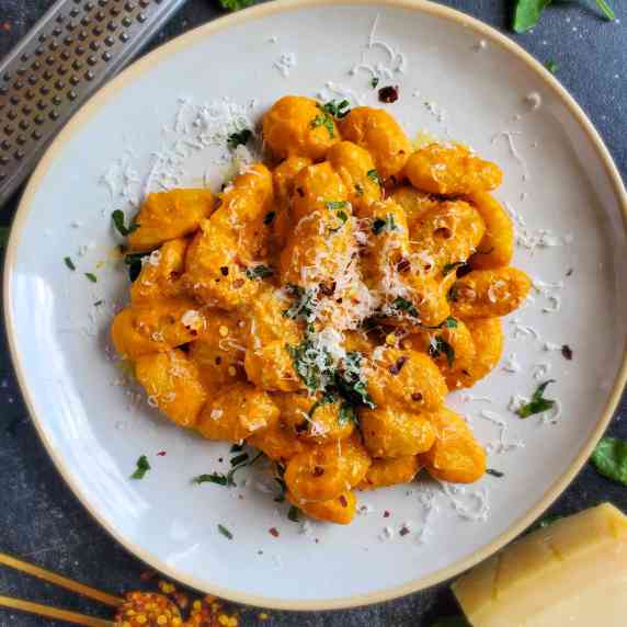 A creamy red sauced gnocchi on a white plate against a black background.