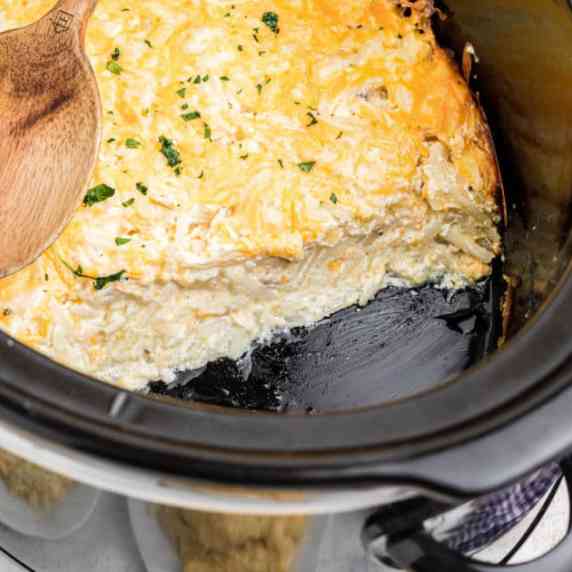 A crock pot with hash brown casserole with some missing.