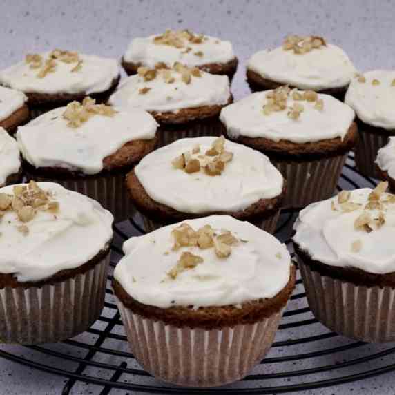 Several carrot cake muffins with mascarpone frosting and chopped nuts on a wire rack