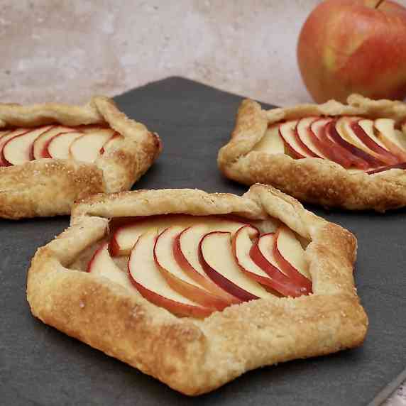 Individual apple galettes on a slate next to an apple