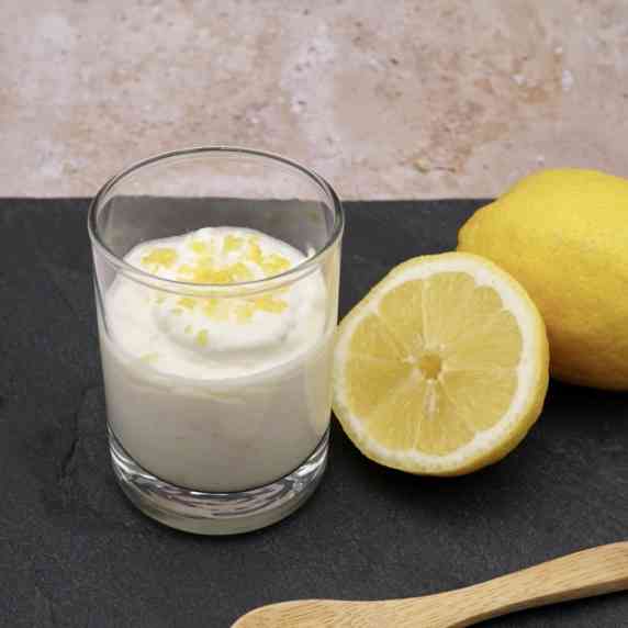 A glass of lemon mousse next to some lemons