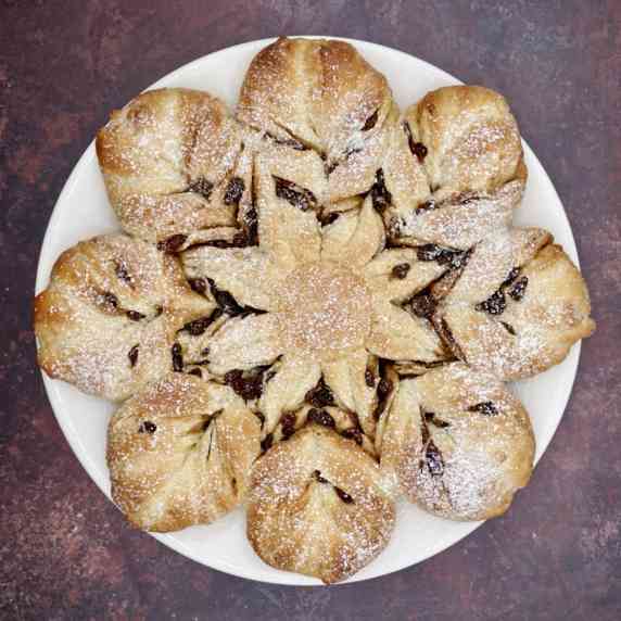 Overhead view of cinnamon star bread dusted with icing sugar on a white plate on a dark countertop. 