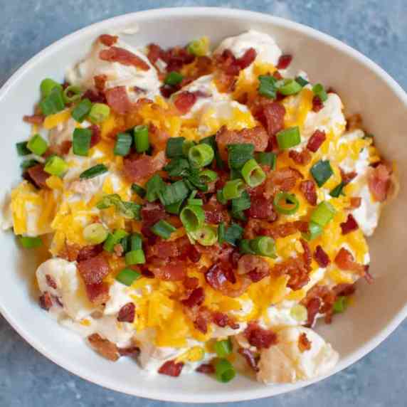 white bowl of potato salad topped with cheddar cheese green onions and bacon