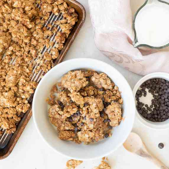 Bowl of gluten-free granola surrounded by chocolate chips and a huge baking pan of granola