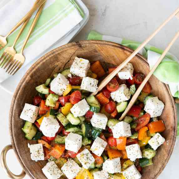 Greek Salad in a Large Wooden Bowl with Gold Forks and a Green Napkin 