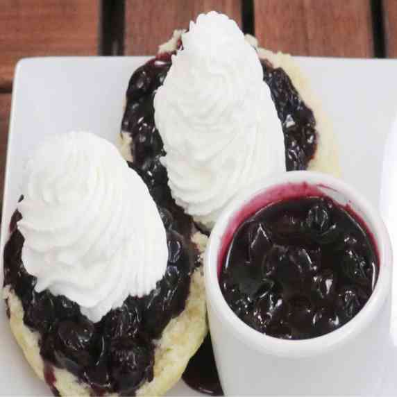 Biscuit topped with blueberry compote and whipped cream with a side of additional blueberry compote.