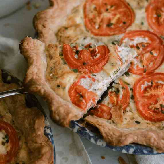 two blue pie plates filled with broccoli goat cheese quiche and topped with tomatoes