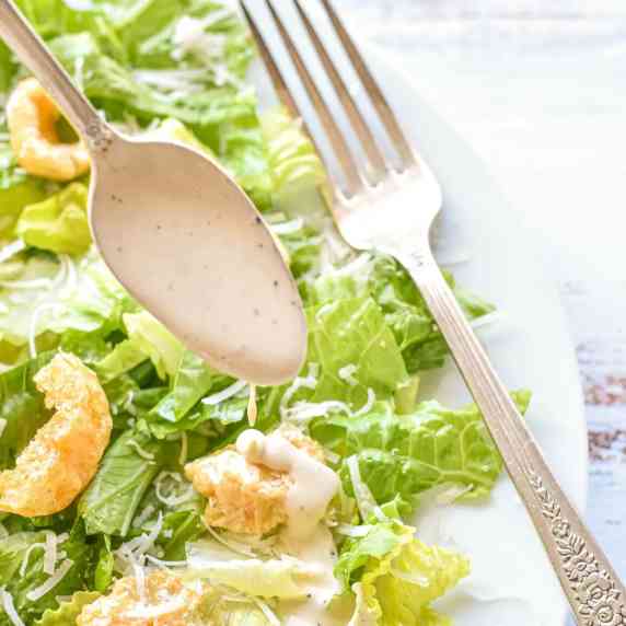 a spoon drizzling low fodmap Caesar dressing onto a salad on a white plate