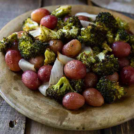 roasted broccoli, roasted grapes, and onions on clay plate set on wood table
