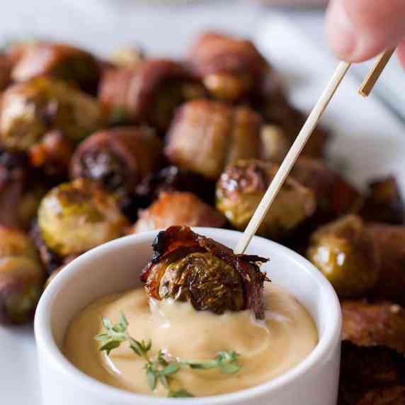 A platter of bacon wrapped brussels sprouts and dish of maple mustard dip.