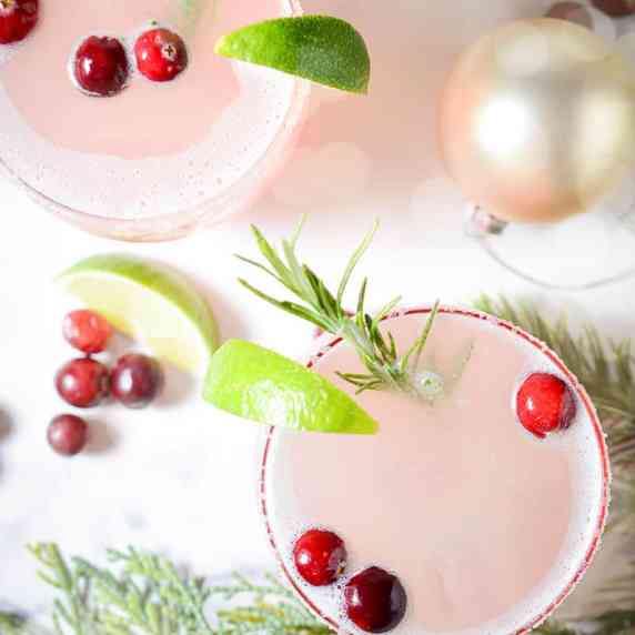 Overhead view of two cocktails with lime, rosemary and cranberry garnishes.