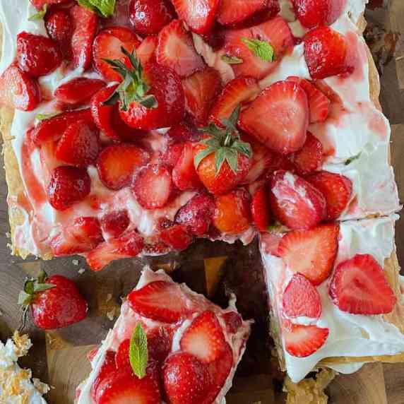 A  large strawberry shortcake dessert made with puff pastry sitting on a wooden cutting board.