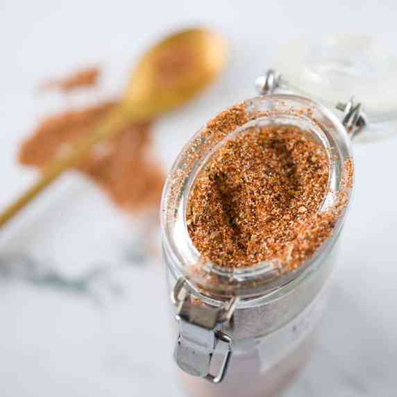 A glass jar on a white counter filled with a blend of spices for tacos.