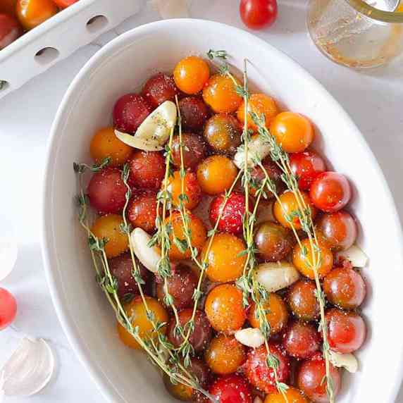 Oval casserole filled with multi-colored cherry tomatoes, sprigs of thyme and garlic cloves.