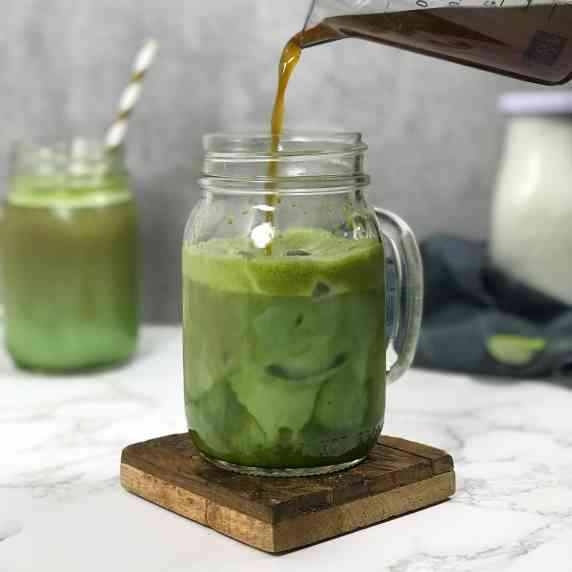 Brown, brewed coffee is poured into a mason glass of green matcha swirling with white milk.