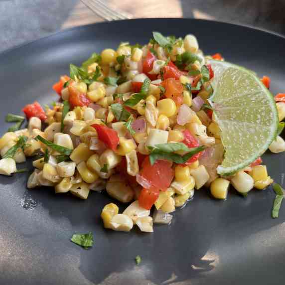 Colorful corn and red pepper salad tossed in a lime vinaigrette served on a black plate. 