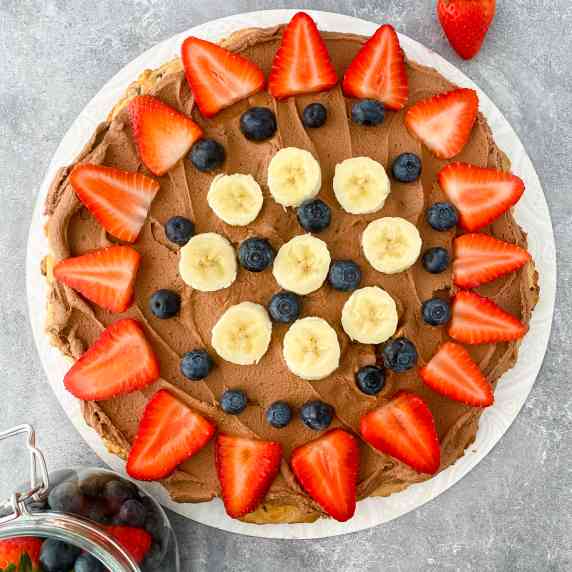 dessert fruit pizza on a plate with strawberries, blueberries, and banana slices
