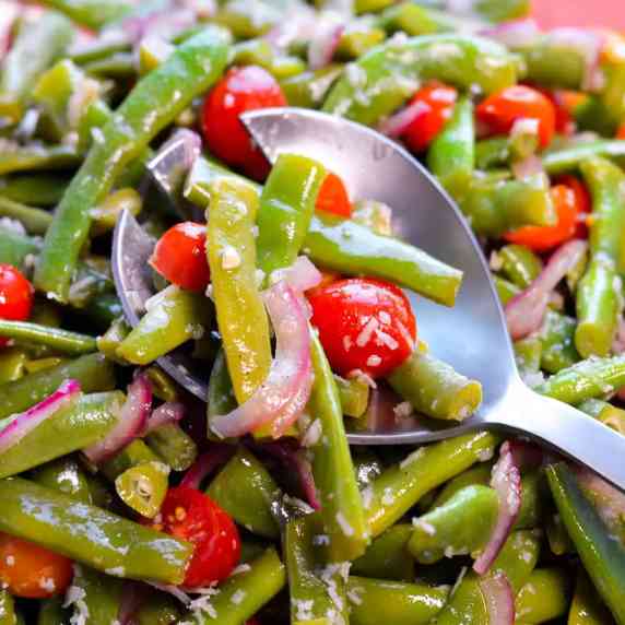 Fresh Green Bean Salad on a silver serving spoon with tomatoes, red onion and parmesan cheese