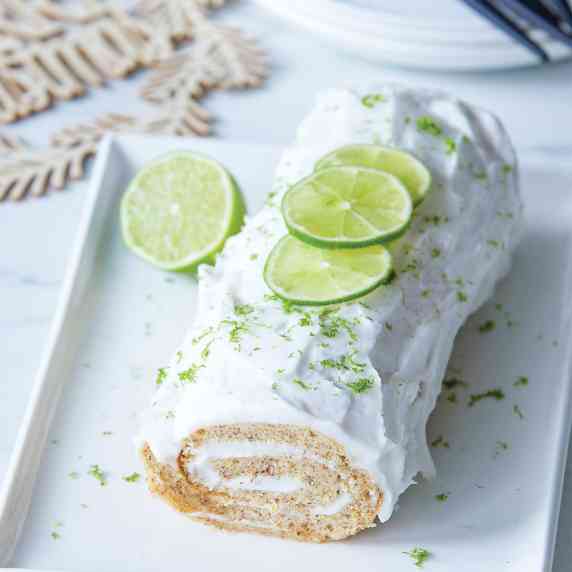 Gin and tonic roulade with freh lime zest sits on a white platter ready to be sliced.