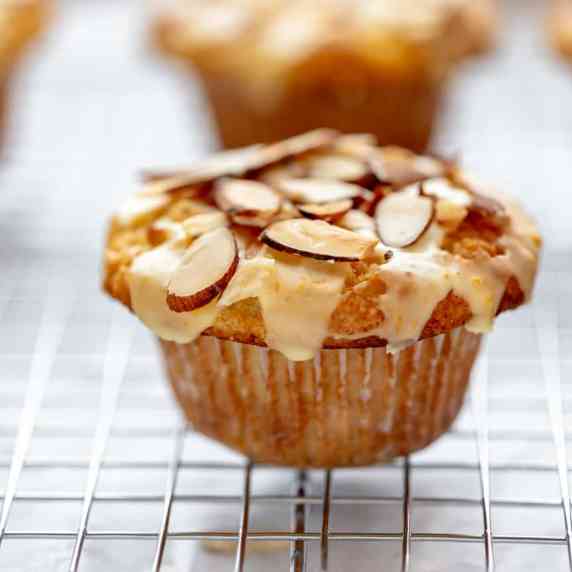 An orange almond muffin with orange glaze and toasted almonds, sitting on a cooling rack.