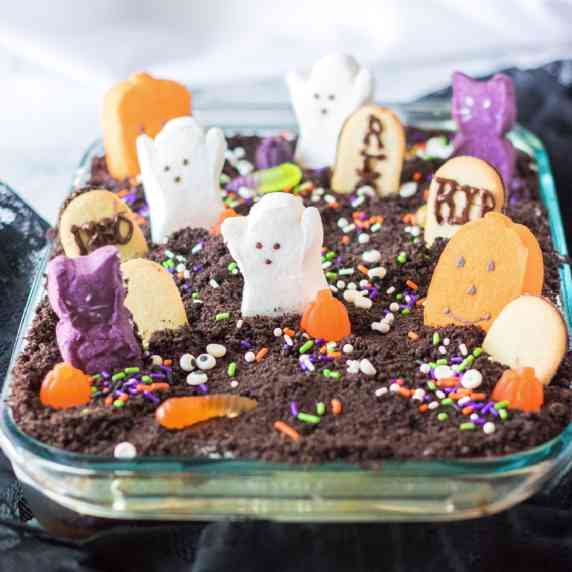 Chocolate ghost graveyard cake in a glass pan from the side decorated with Halloween themed candy.
