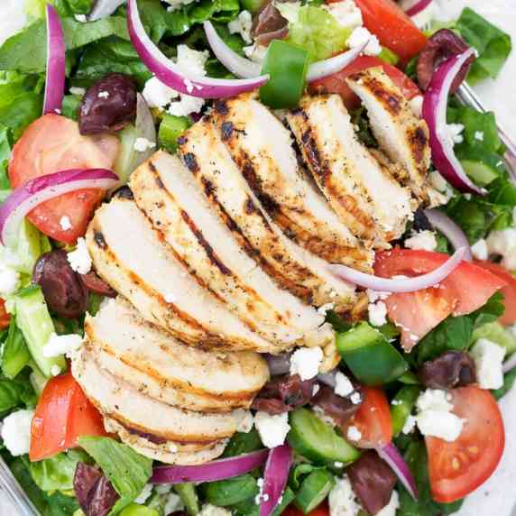 Greek salad topped with grilled chicken breast.