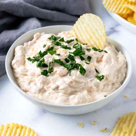 Greek Yogurt French Onion Dip in a white bowl with a potato chip in it.