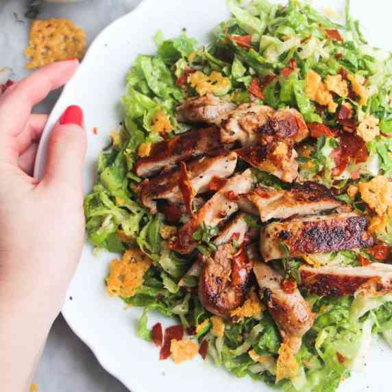 Hand holding a plate of grilled chicken caesar salad.