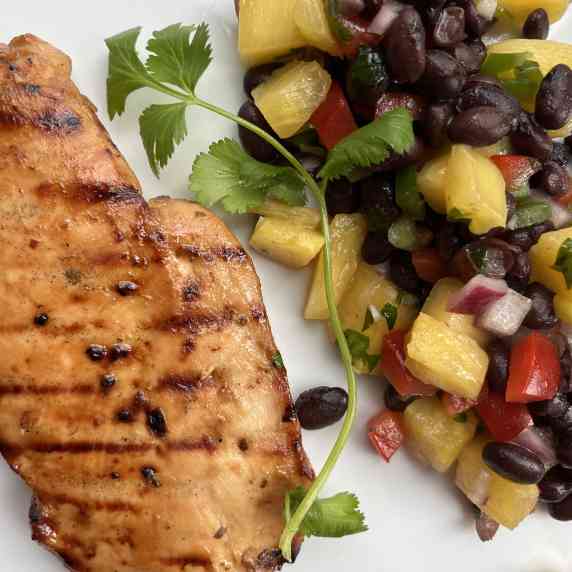 Grilled teriyaki chicken breast with pineapple and black bean salsa served on a white plate.