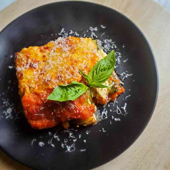 A gorgeous piece of lasagna dredged in a red sauce on a black plate.