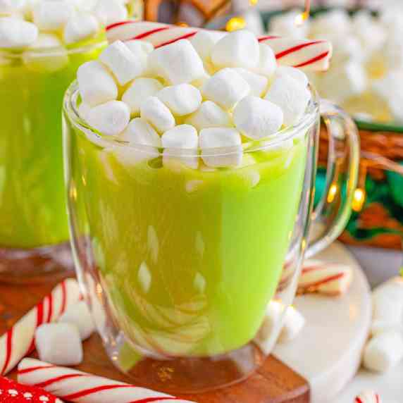 Close view of a cup of green hot chocolate with mini marshmallows and a peppermint stick on top.