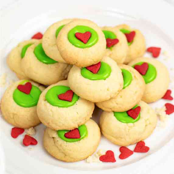 Close up of a stack of thumbprint cookies with a Grinch bright green center with a heart sprinkle.