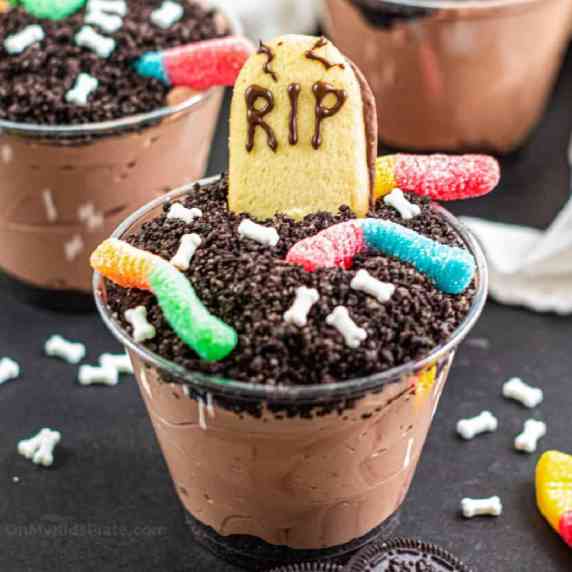 Chocolate dirt pudding cup decorated with gummy worms, bone sprinkles and a cookie headstone.