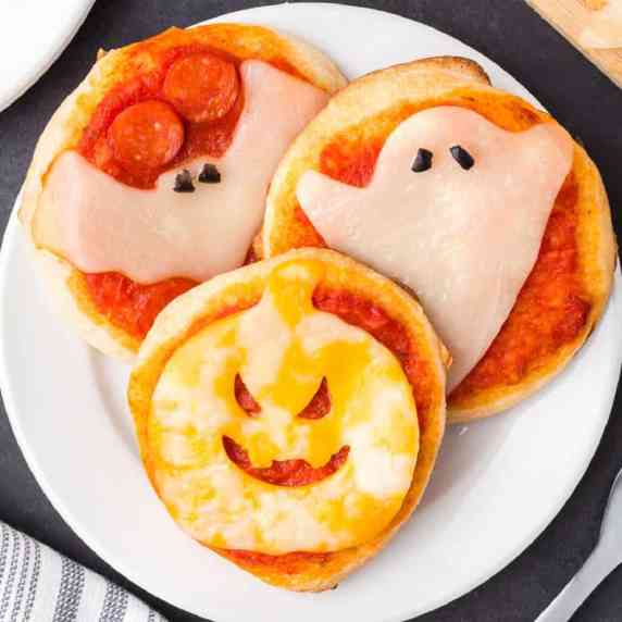 Mini pizzas decorated with cheese slices shaped to look like a bat, ghost and jack-o'-lantern.