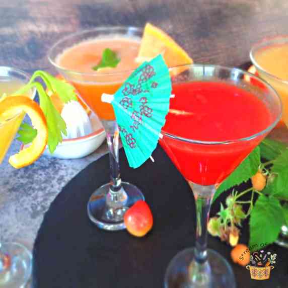 Four fruit mocktails on a black circular board with fresh fruit in the background